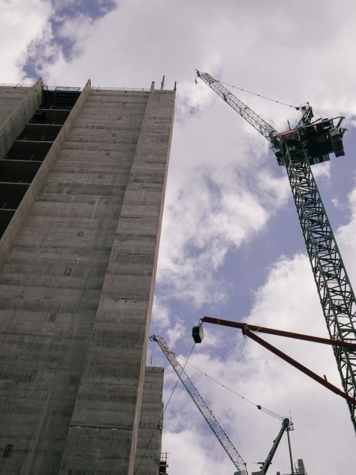 about-01 Low angle view of skyscraper under construction with cranes against blue sky.