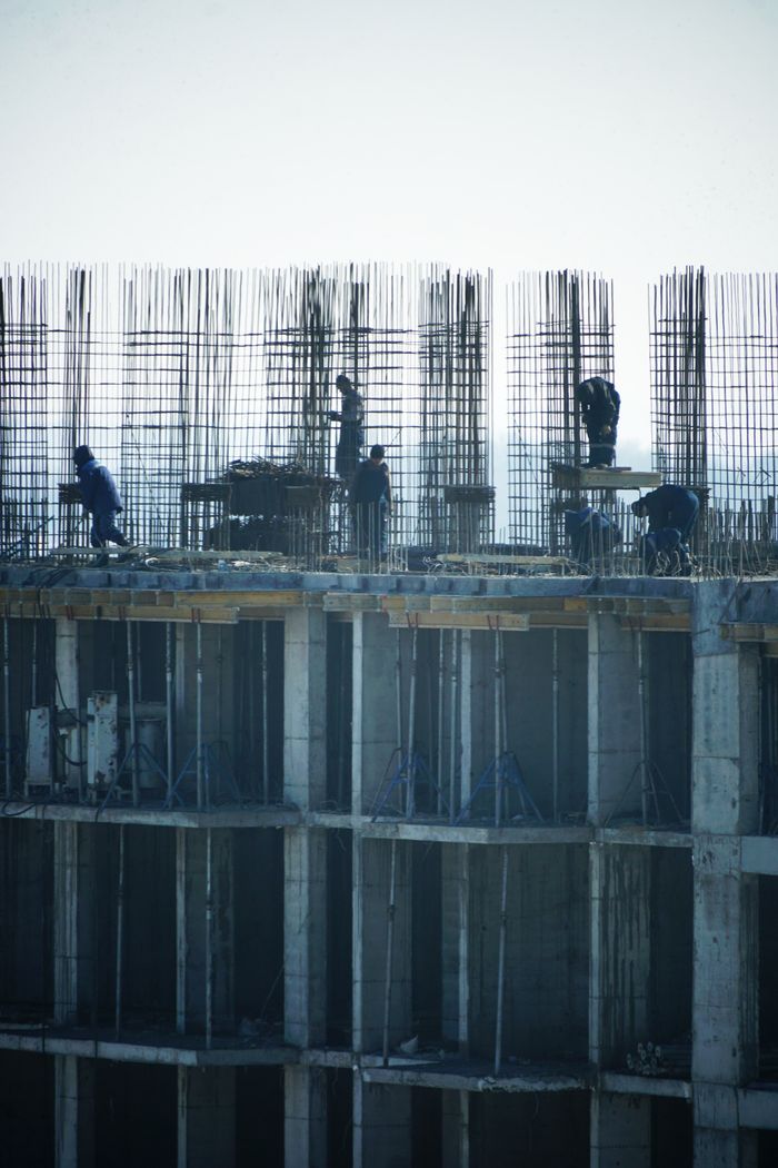 why-choose-us-02 Construction workers at a high-rise building site with visible steel reinforcements.