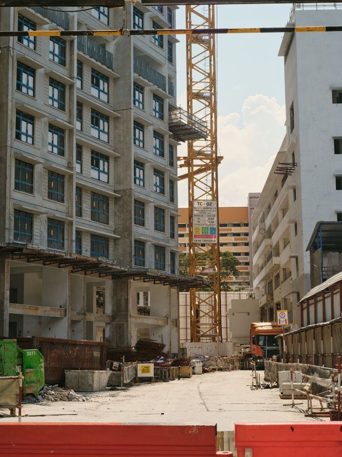 about-02 A bustling urban construction site with a tower crane and surrounding buildings under a clear sky.