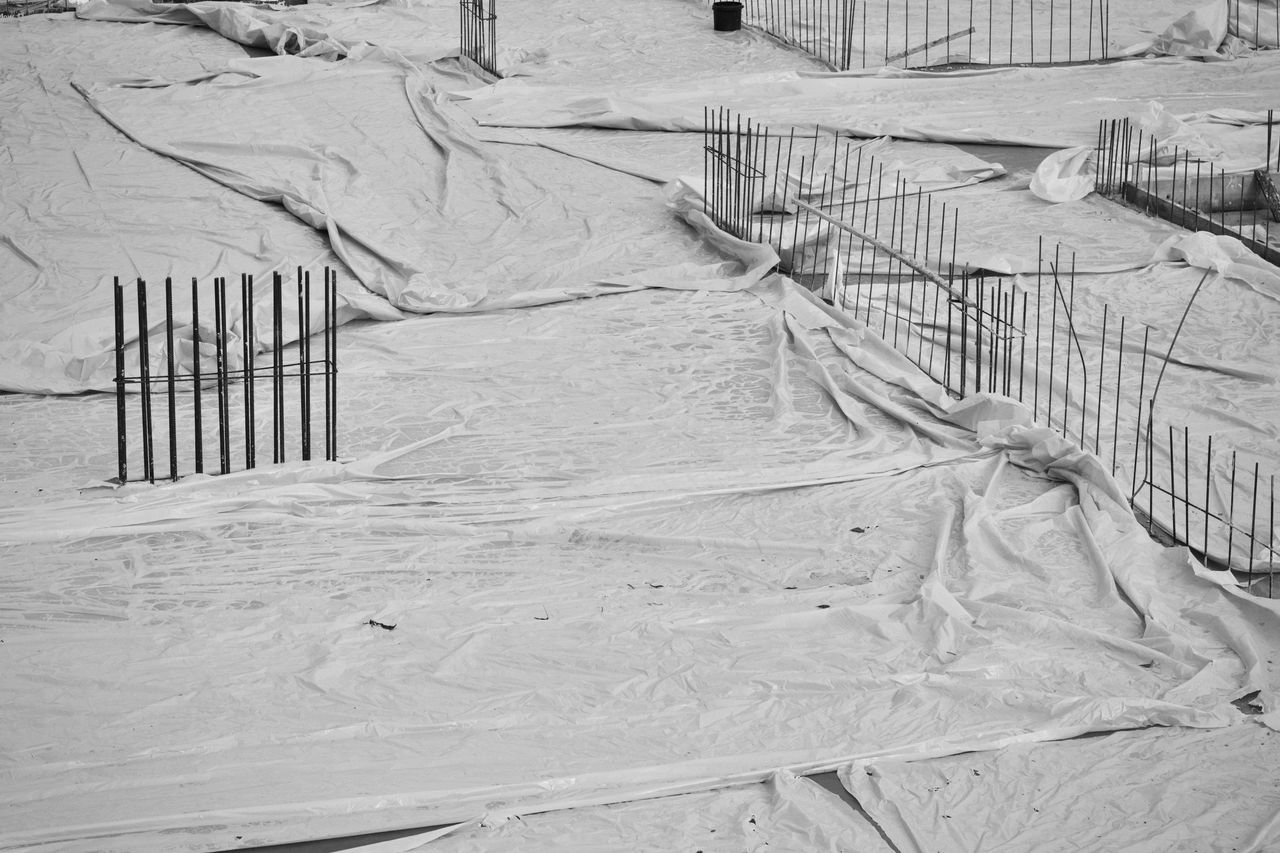 services-01 Monochrome image of a construction site with foundations covered by sheets and exposed rebar.