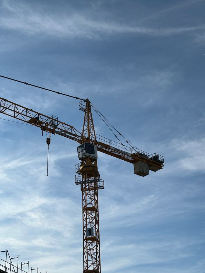 why-choose-us-03 Tall tower crane at a construction site with a clear blue sky background, showcasing construction industry machinery.