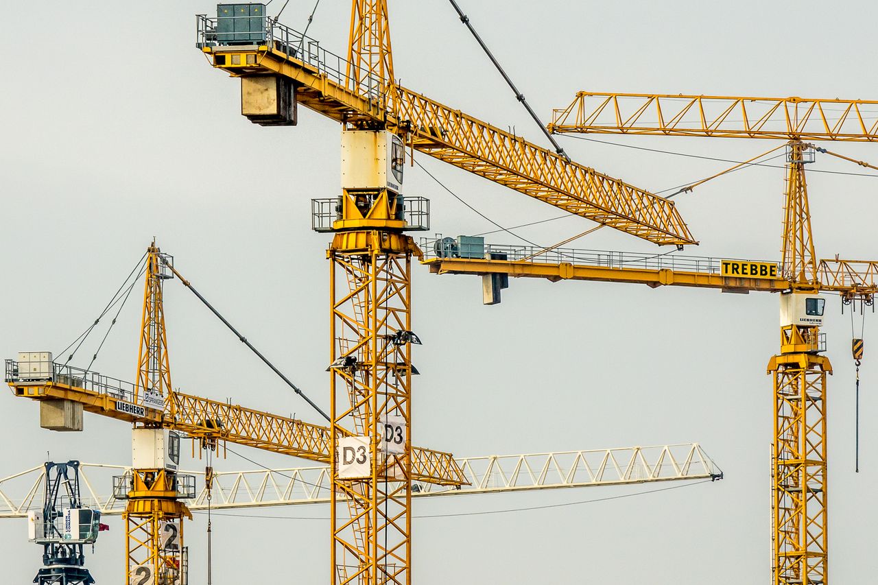 hero-02 Cluster of yellow tower cranes at a construction site with a gloomy sky background.