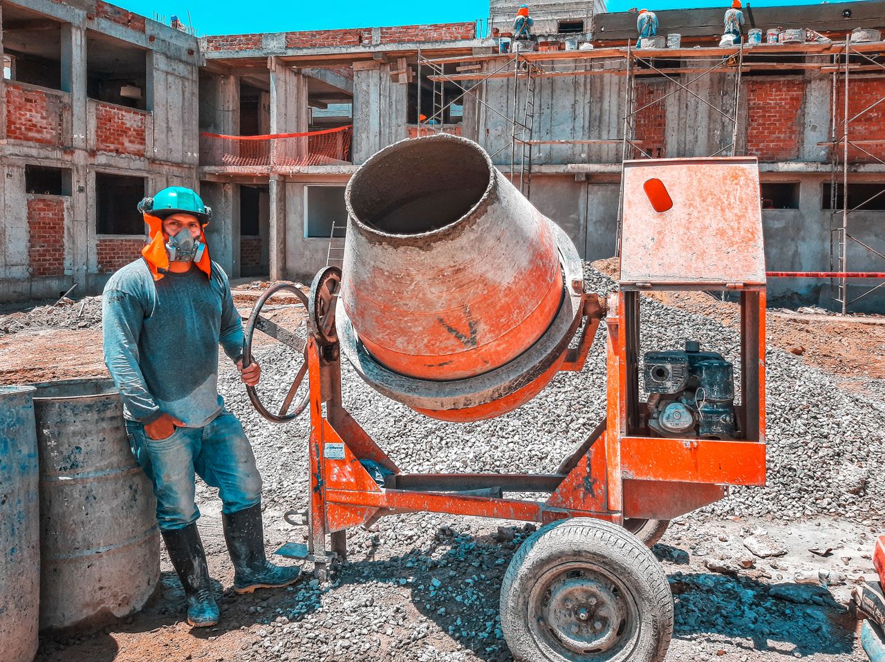 hero-01 A construction worker operating a concrete mixer at an active building site, emphasizing safety gear.